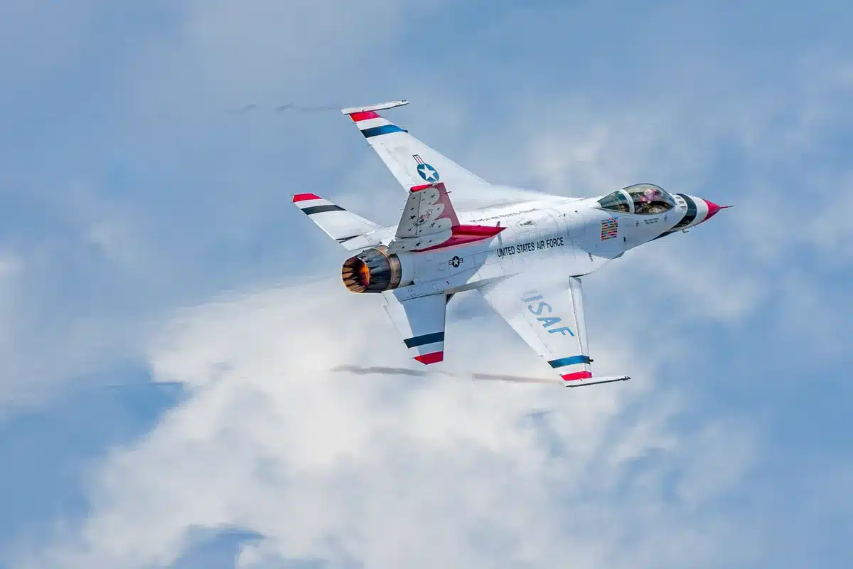Military jets in tight formation against a clear sky, gray and blue aircraft banking in synchronized precision, spectators watching from below, afternoon sunlight catching the fuselages