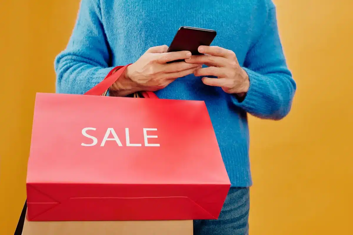 A busy retail storefront with shoppers browsing racks of discounted clothing and home goods, warm overhead lighting illuminating rows of merchandise, customers in motion examining items, the store interior filled with activity and energy.