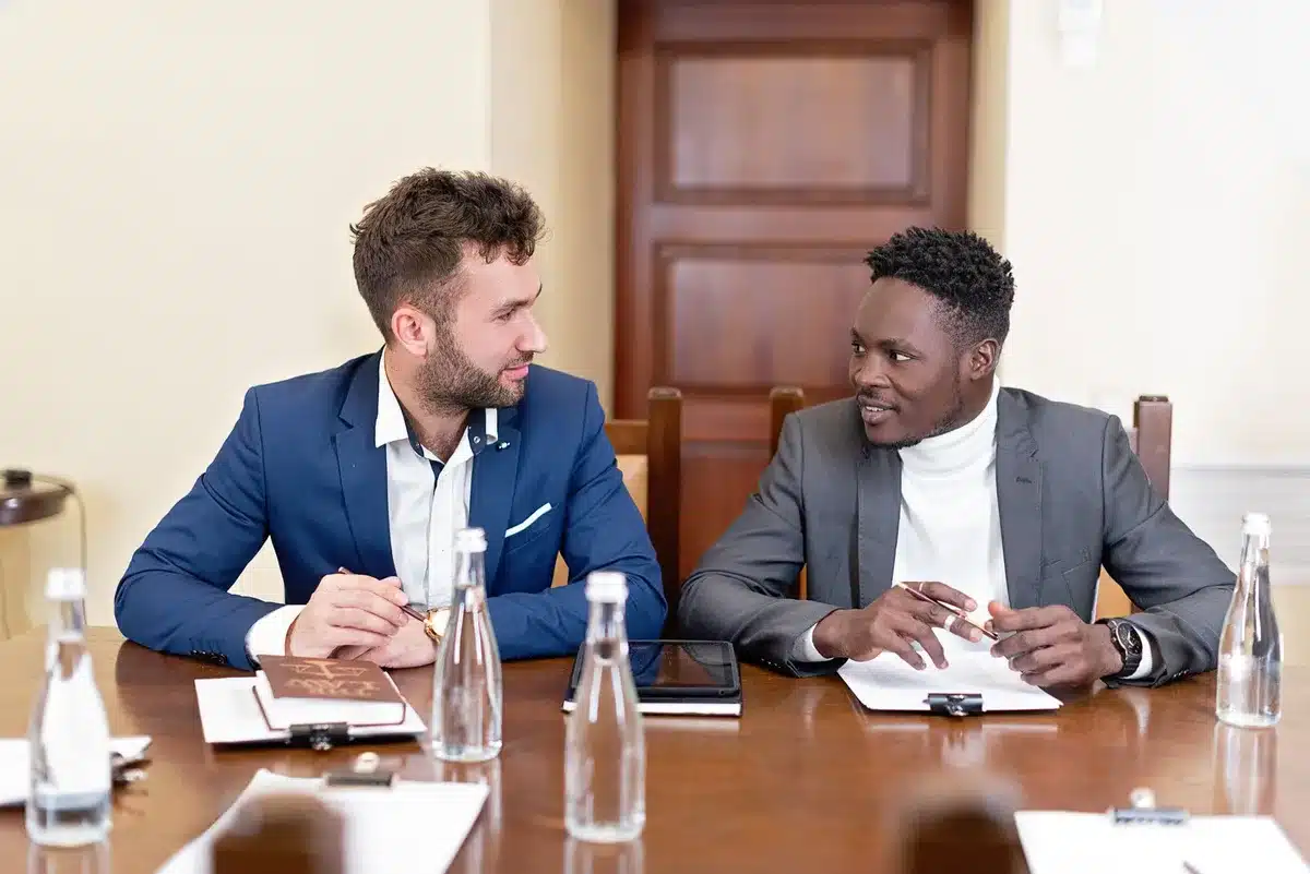 Diplomats in formal attire seated across a negotiation table with national flags visible in soft focus, papers and water glasses arranged before them, a moment of tense discussion frozen in time.