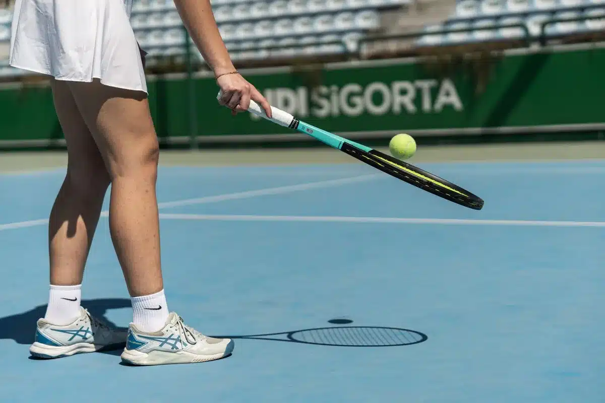 A tennis player mid-rally on a hard court, racket extended after striking the ball, hard-court surface and net visible, focused intensity