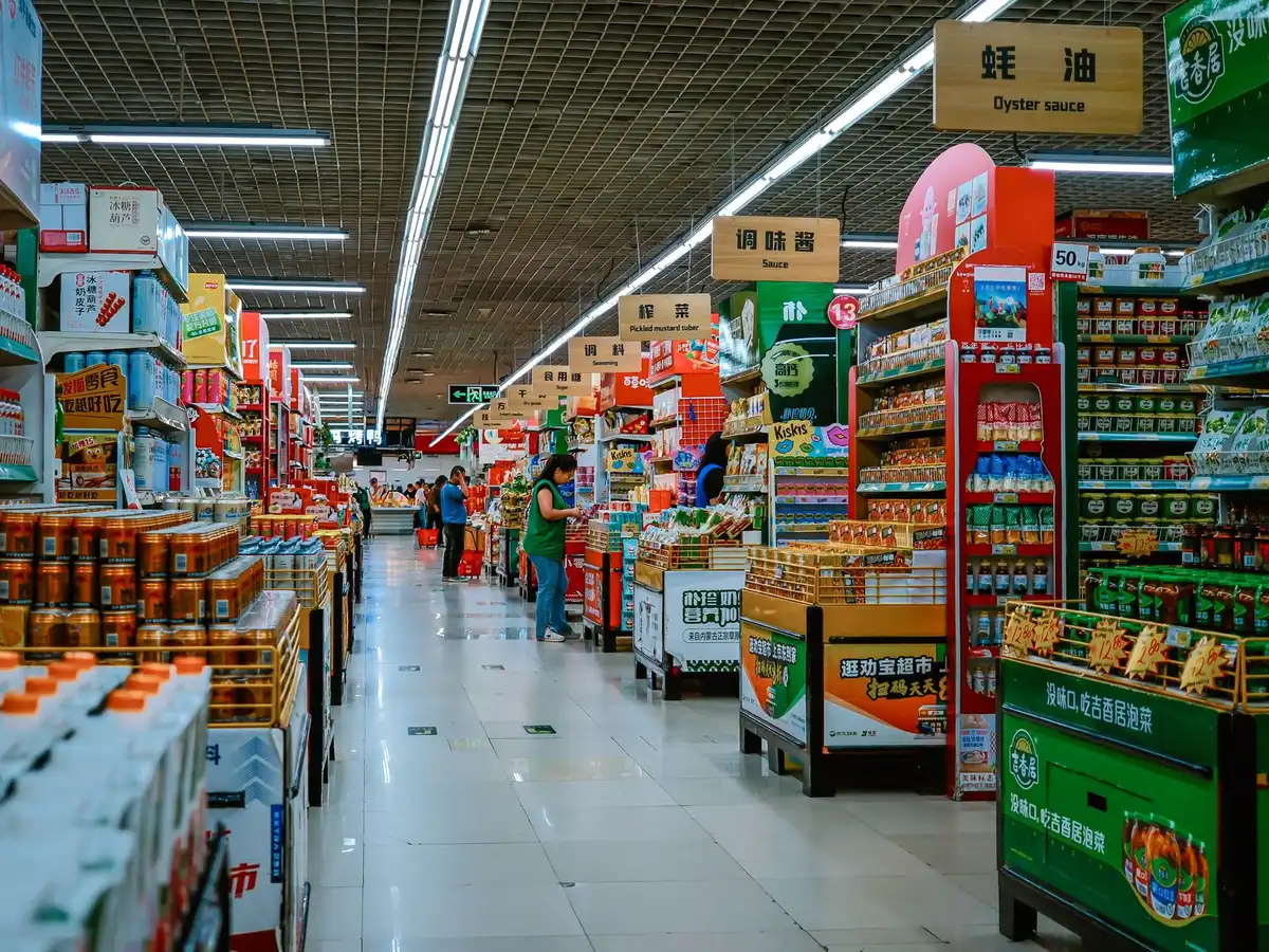 An empty or partially stocked grocery store aisle with shelves and fluorescent lighting, representing the interior of a restructuring retail space during a transition period.