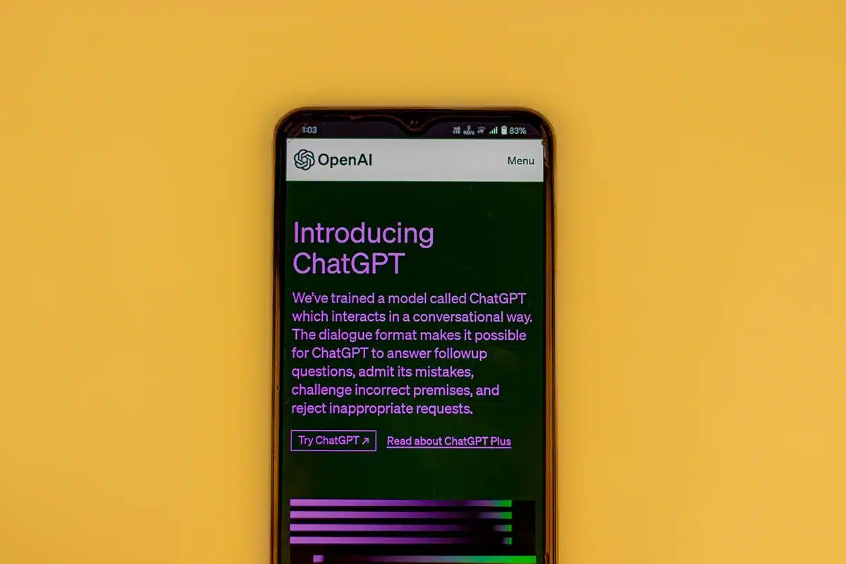 A close-up of a smartphone screen displaying a chat interface with glowing text, casting blue light on blurred hands in the background, surrounded by darkness.