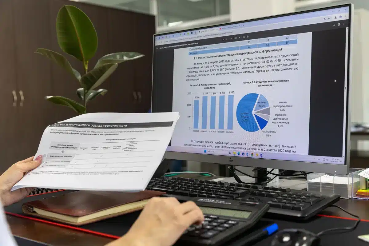 An empty office chair at a desk with scattered financial documents and a computer screen showing account information, cool overhead lighting, symbolizing the administrative machinery of debt collection.