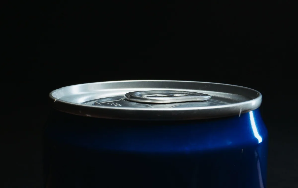 Close-up of aluminum can seam and base, magnified to show potential weakness point where pressure could cause failure, metallic surface texture detailed
