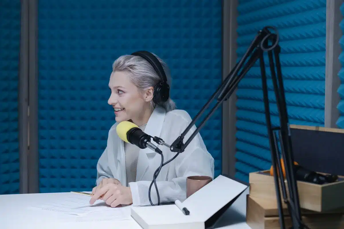 A professional political commentator in a broadcast studio setting, speaking at a desk with microphones and news graphics visible in soft focus behind him, conveying authority and media presence