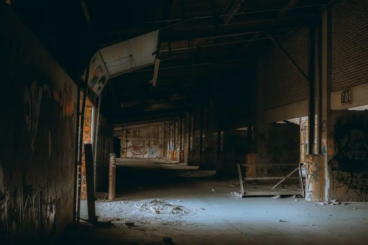Empty warehouse or storage facility with rows of empty spaces and dim lighting, suggesting loss and absence of assets, with abandoned office furniture in the background