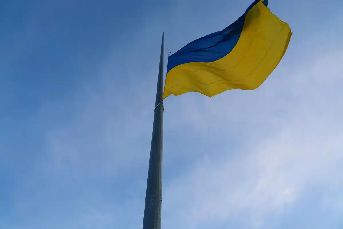 A split-screen composition showing a Ukrainian flag on one side and an abstract representation of economic sanctions or tariffs on the other, symbolizing the economic pressure the bill aims to apply.