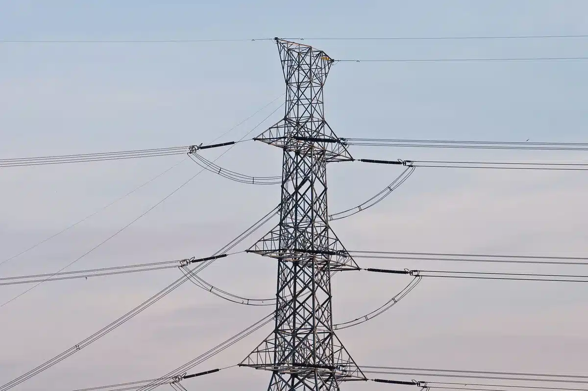 A power grid transmission tower at sunset with storm clouds gathering, representing energy infrastructure and grid capacity concerns.