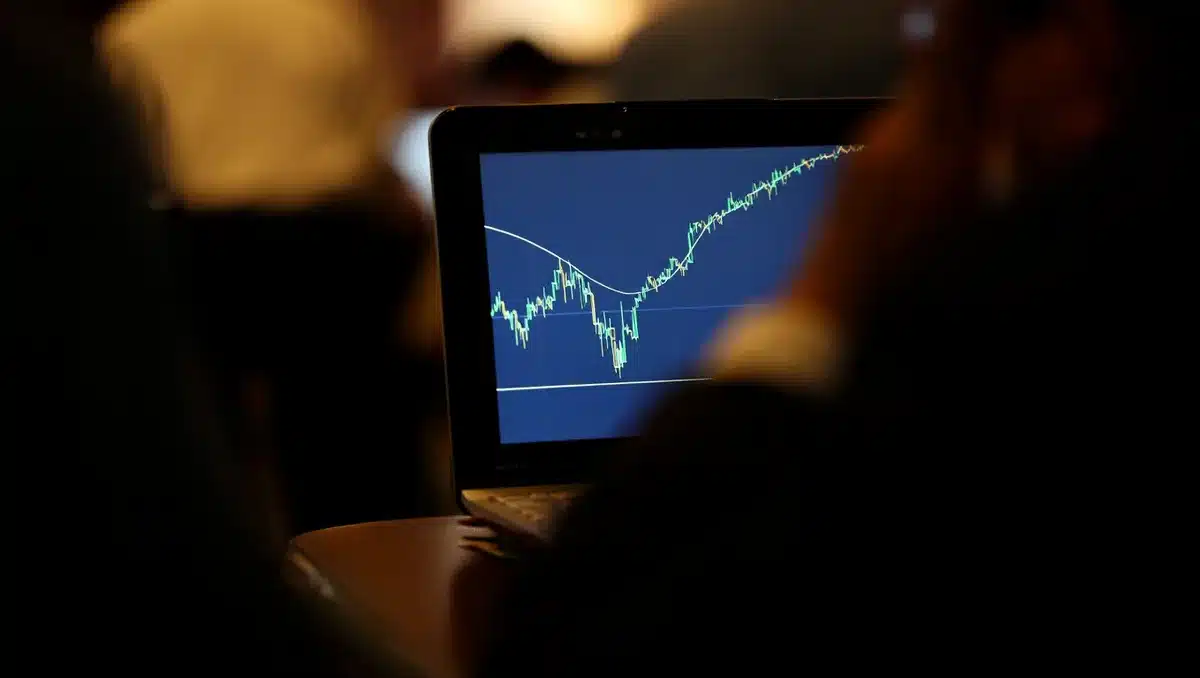 A stock market ticker display showing rising price chart with green candlesticks and upward trend line, illuminated by monitor glow in a dark trading environment | stock market growth chart