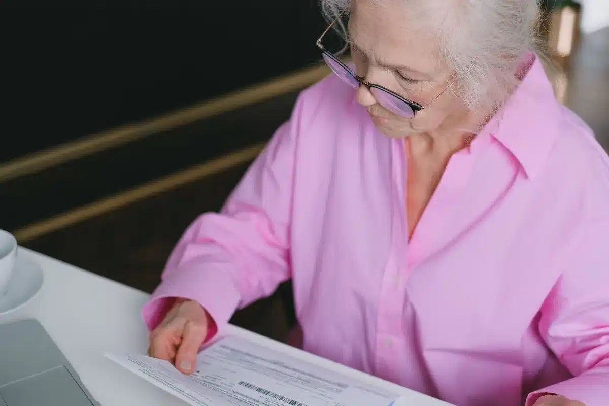 An elderly person reviewing financial documents at a table, reading a letter about benefit changes, soft natural light illuminating the paperwork and their focused expression