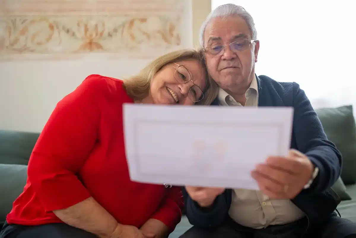 A retiree reviewing financial documents and a Social Security statement at a kitchen table with a calculator and reading glasses nearby