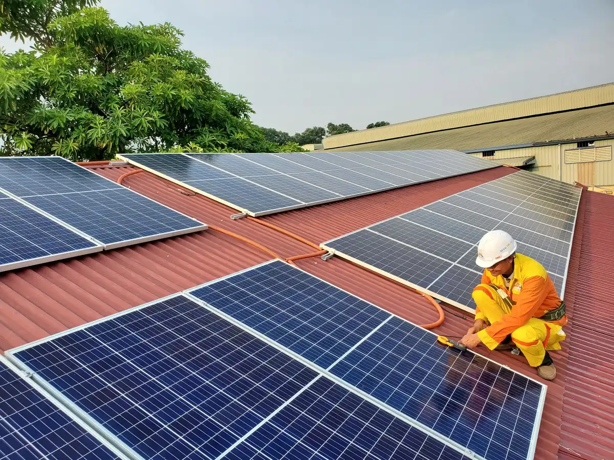 Rows of solar panels in a utility-scale installation at dusk, golden light reflecting off glass surfaces, with a technician silhouette in the foreground inspecting equipment.