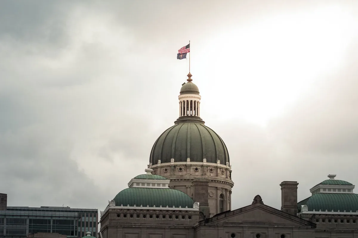 A South Carolina state capitol building exterior framed against a clear sky, official flags at the entrance, mid-morning light