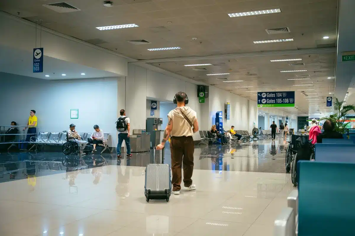 Airport terminal gate area with boarding passengers in background, one empty seat in foreground with a luggage tag, warm amber lighting, sense of anticipation