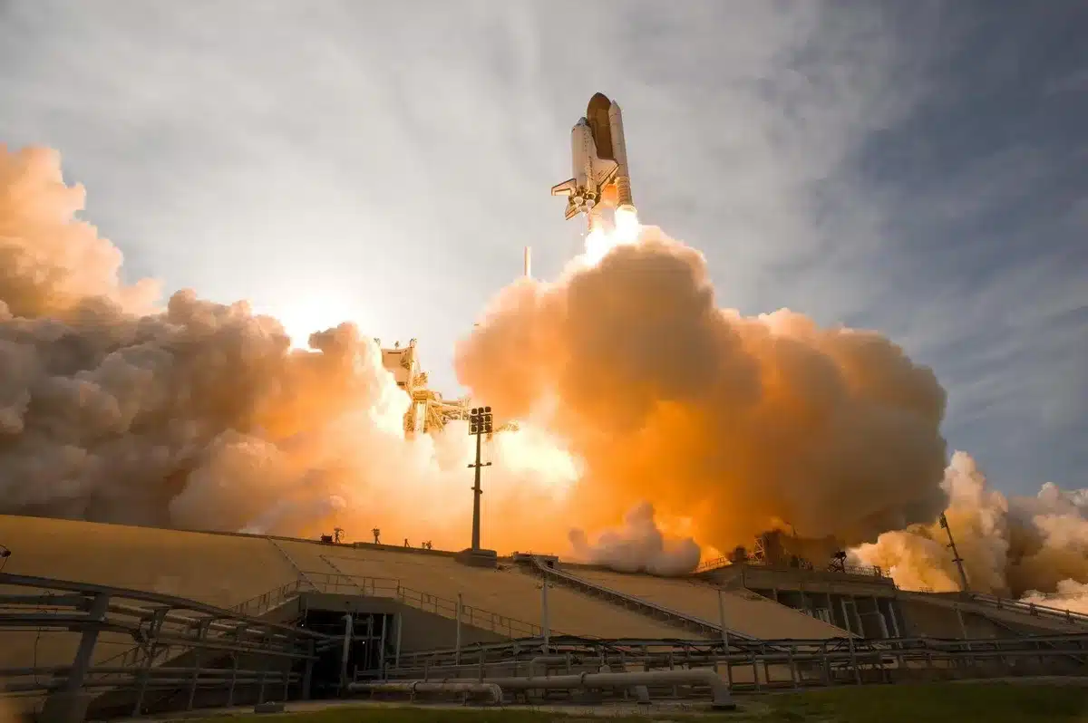 A Falcon 9 rocket on its launch pad at dusk, bathed in golden floodlights, with the gantry structure framing the vehicle against a darkening Florida sky, the Atlantic horizon visible in the distance.