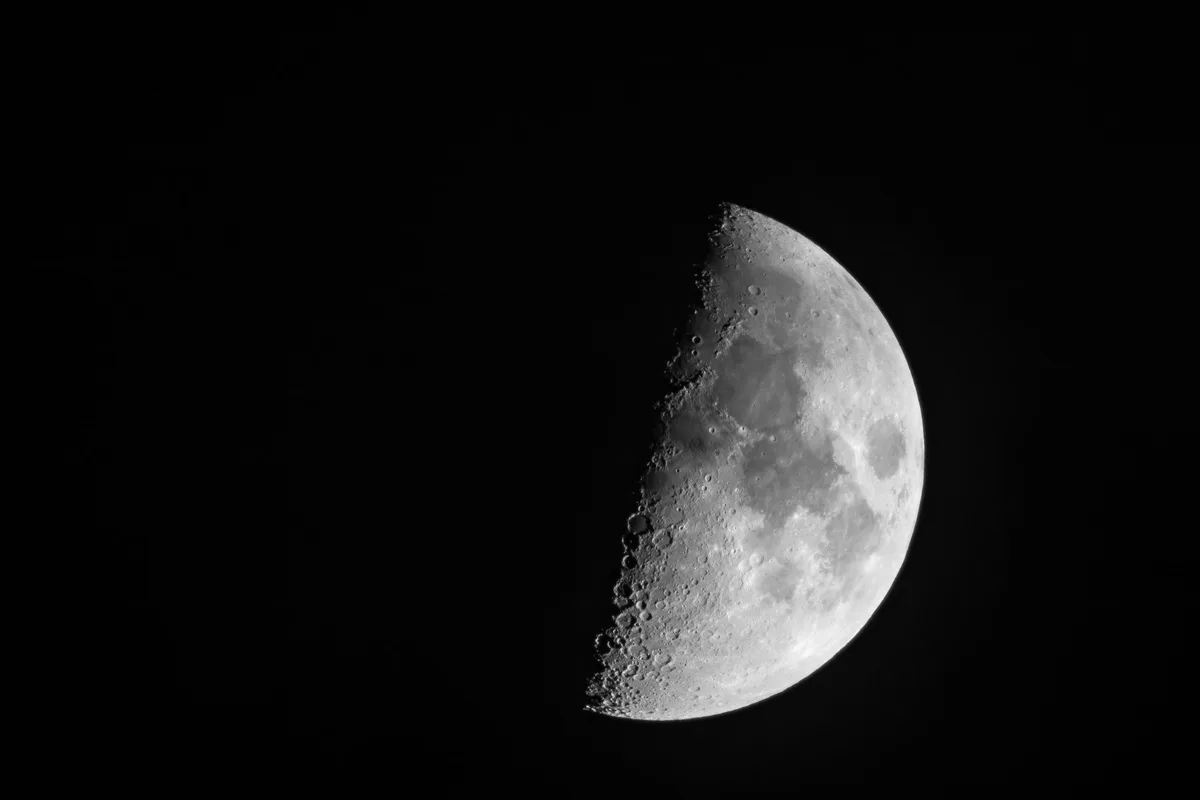 A fresh crater on the moon's surface with ejected dust and rock debris radiating outward in a star pattern, the rim still sharp and bright against darker lunar regolith — power.