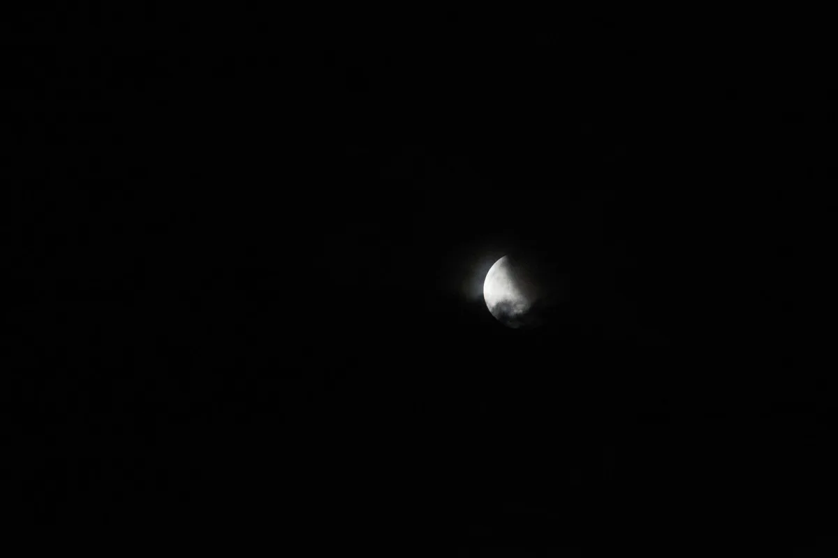 A spent rocket upper stage tumbling silently through the vacuum of space, solar panels glinting faintly against the star field, approaching a crescent moon in the distance.