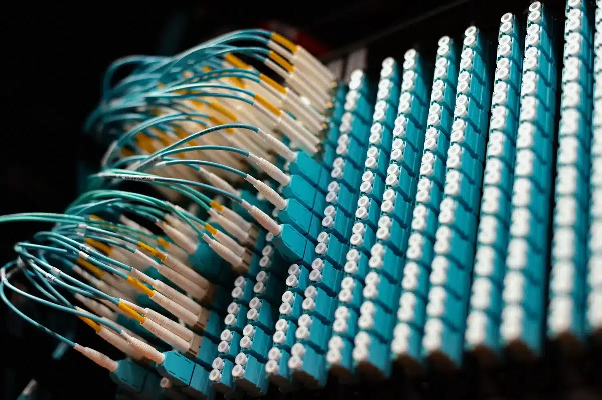 A sprawling data center facility with rows of server racks glowing with blue and white lights, massive cooling systems, endless cables and infrastructure stretching into shadows, technological scale and power