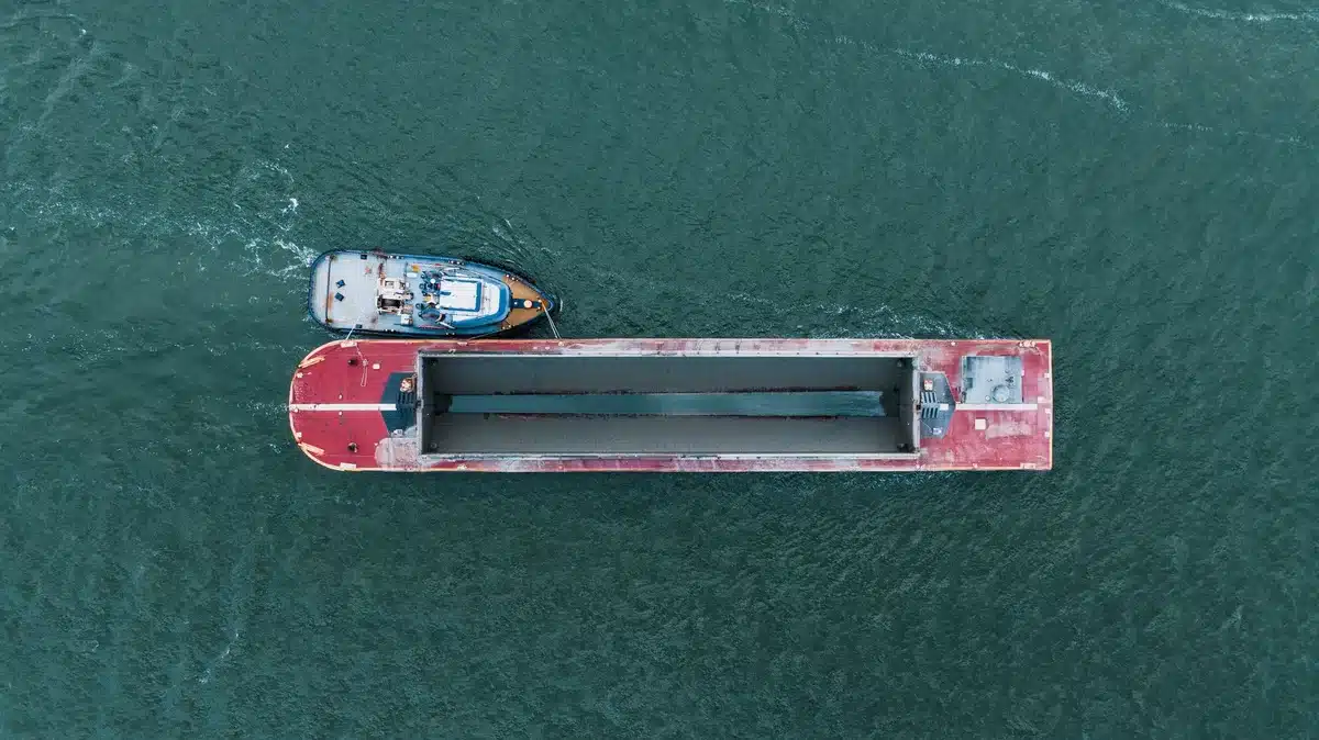 A droneship cutting through ocean waves with recovery equipment ready on deck, under overcast sky.