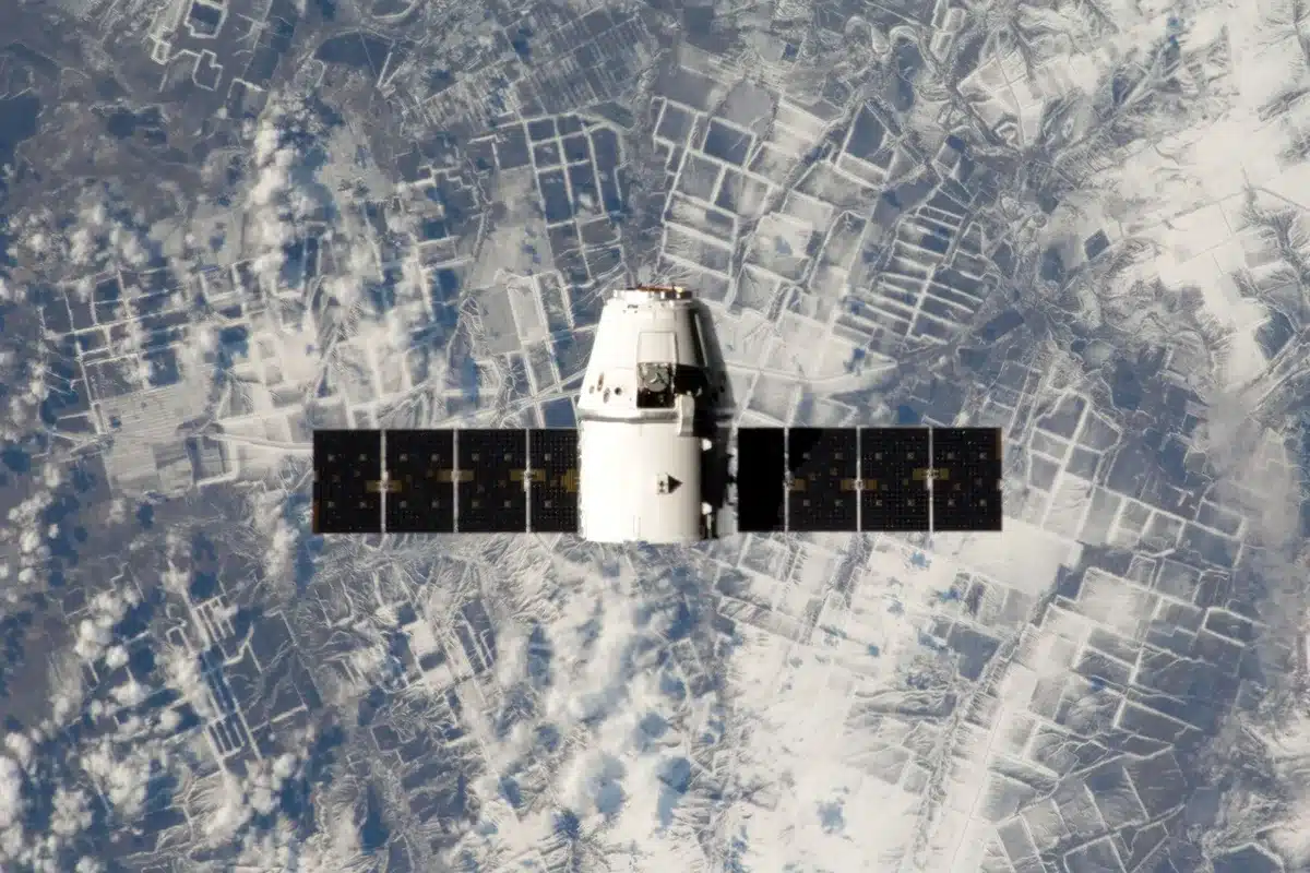 A spacecraft floating upright in calm blue ocean water, still steaming from reentry, with the horizon and sky visible in the background under daylight.