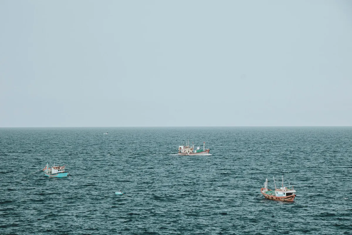 A spacecraft floating intact in calm ocean waters, its metallic hull reflecting sunlight, surrounded by recovery vessels and small boats approaching from a distance.
