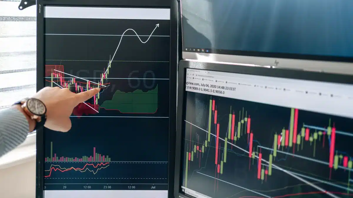 Stock trading floor with multiple screens displaying green upward-trending charts and financial data, traders monitoring positions, morning sunlight through windows