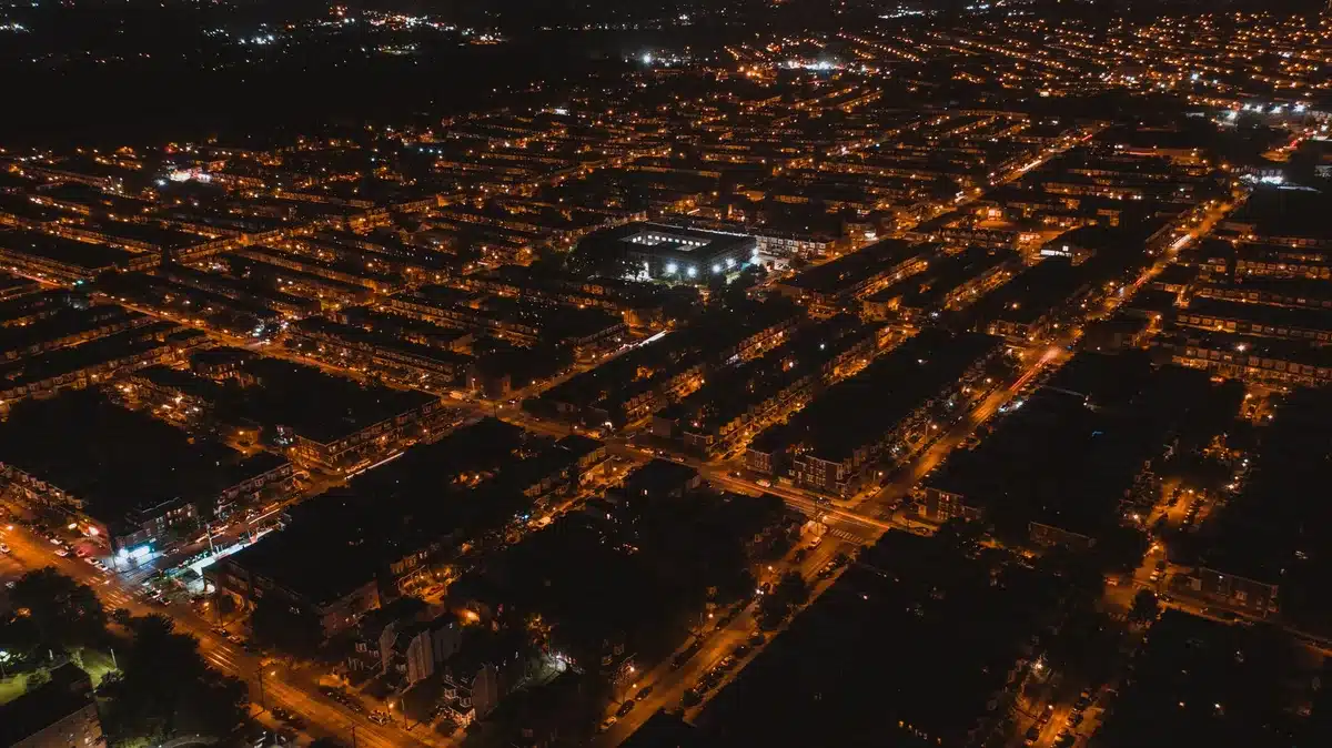 A darkened residential street at evening with streetlights off, traffic signals unlit at an intersection, silhouettes of homes against a dimly lit sky, power lines visible overhead against the darkness