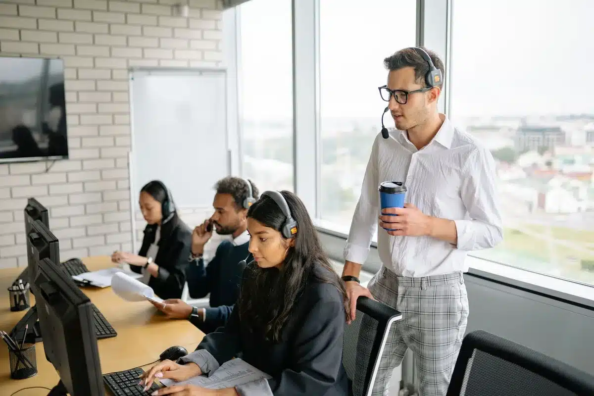 A modern corporate office with rows of desks and computer monitors, a few employees working, natural light from large windows, a sense of ongoing operations before transition
