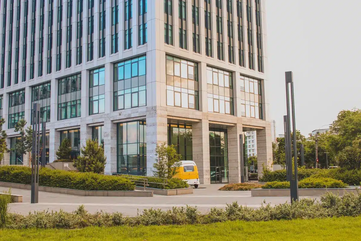 A modern office building exterior reflecting blue sky, State Farm signage visible, customer service representatives working at desks visible through windows, morning light