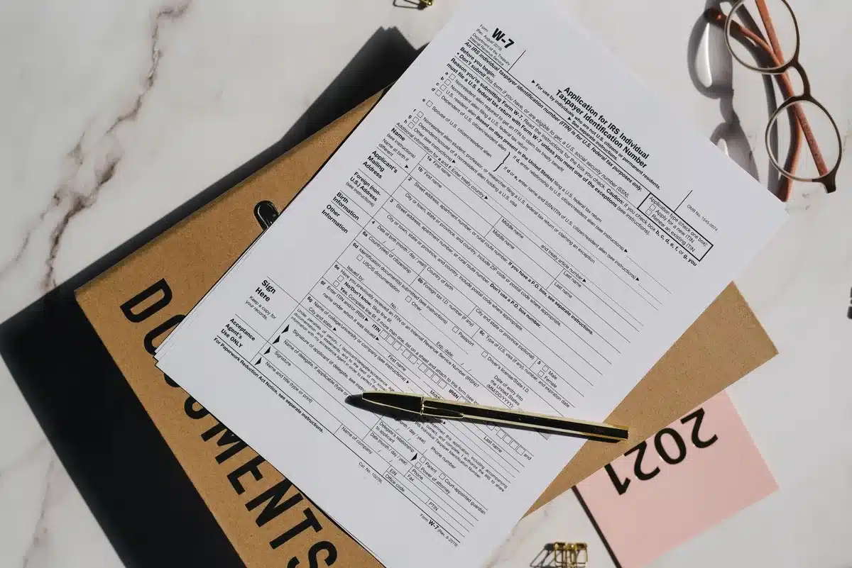 A close-up of a borrower defense claim form being filled out, with a pen hovering over checkboxes, symbolizing the lengthy application process for debt relief.