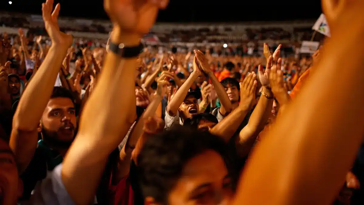 Campaign rally crowd of anonymous supporters with raised arms under stadium lights, faces distant or blurred, energy and motion visible, cheering silhouettes | political rally crowd