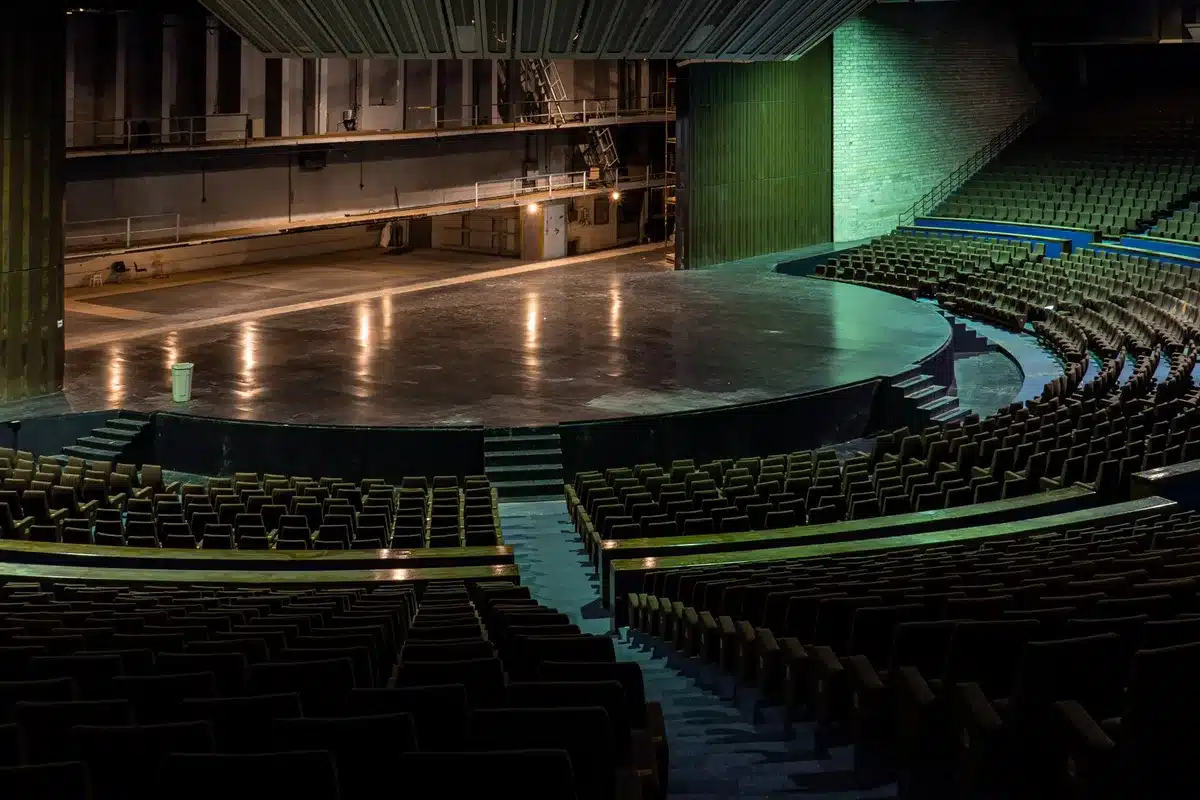 HBO television studio stage with empty roundtable chairs and microphones, warm lighting on the set, the show's backdrop visible, anticipatory atmosphere