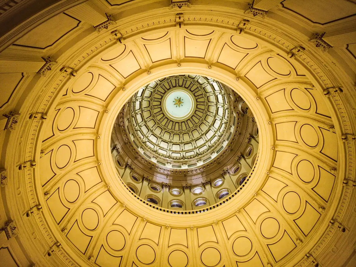 An empty state capitol building interior with morning light streaming through windows, a lone gavel on the governor's desk catching sunlight, symbolizing the historic transition ahead