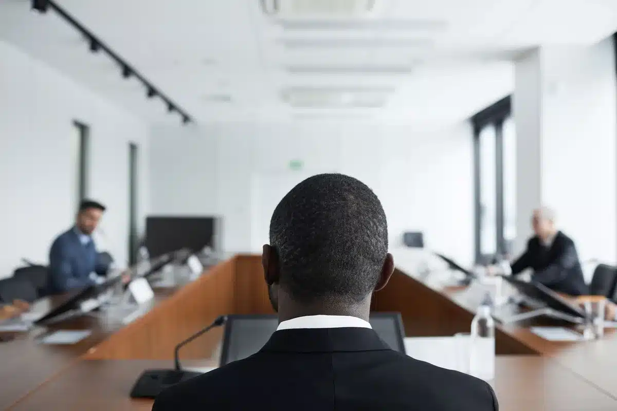 An empty boardroom with a single vacant chair at the head of a long table, morning light streaming through floor-to-ceiling windows.