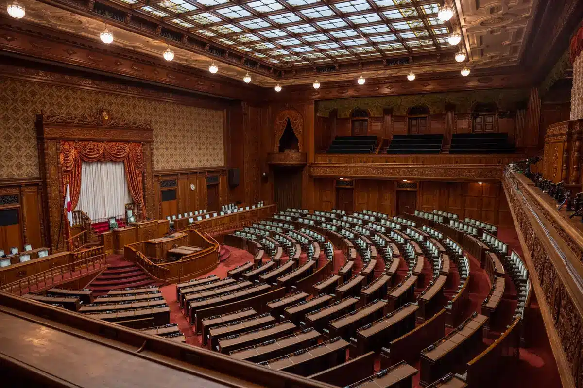 Congressional chamber interior with empty desks and overhead lighting, a single majority leader's seat prominent in the foreground, tension in the austere architecture