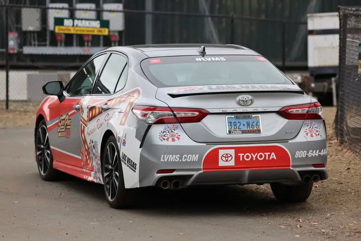 A Toyota Camry Hybrid parked in a service bay with open hood, dealer technician in background, professional automotive setting