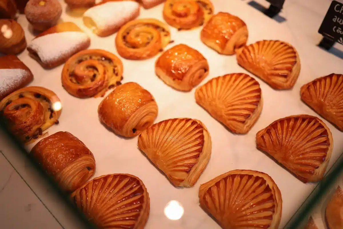 A Trader Joe's bakery section display with multiple Danish pastries arranged on shelves, warm overhead lighting, customers browsing in soft focus