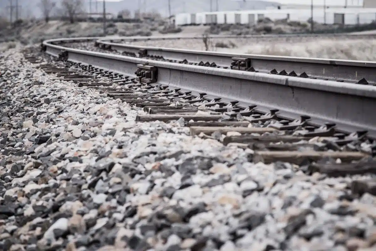 Railroad tracks damaged and misaligned from derailment, close-up of twisted metal rails and wooden ties, emergency equipment nearby, daylight showing track damage extent.