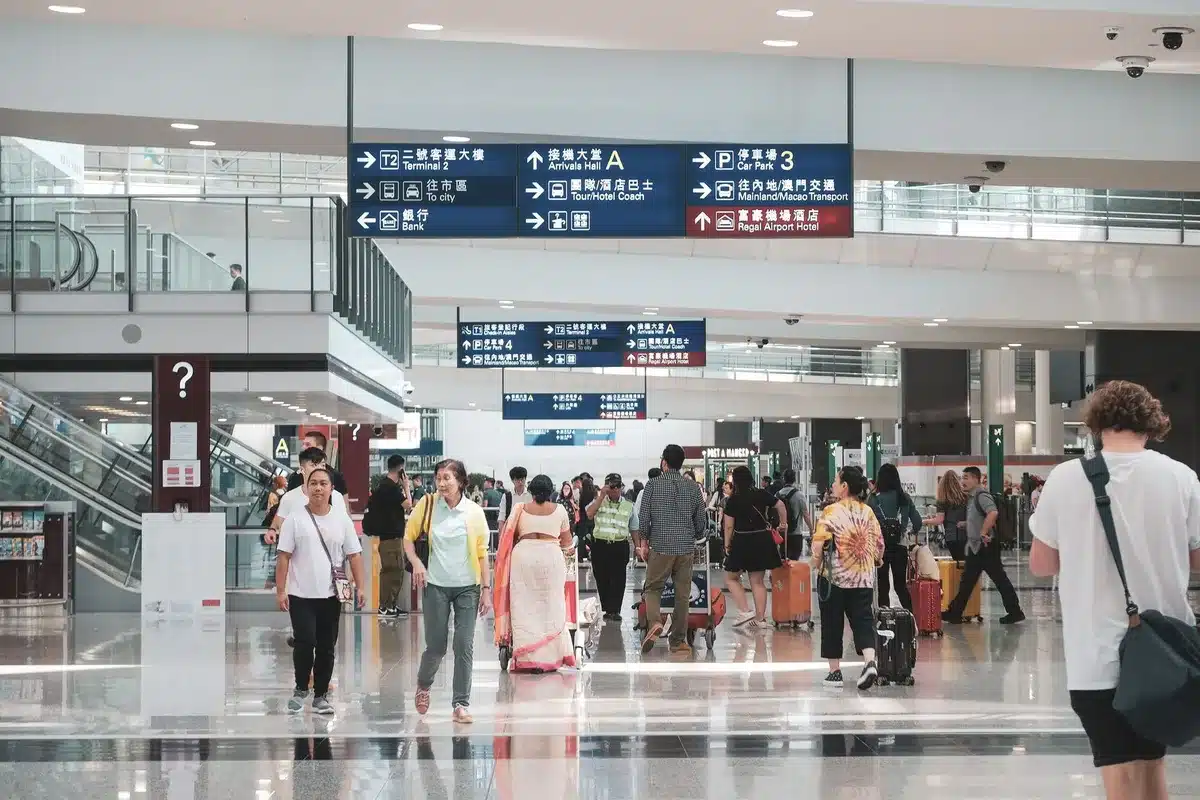 An airport departure board displaying flight cancellations and delays in red text, with travelers standing below looking at the screen in concern, bright terminal lighting overhead