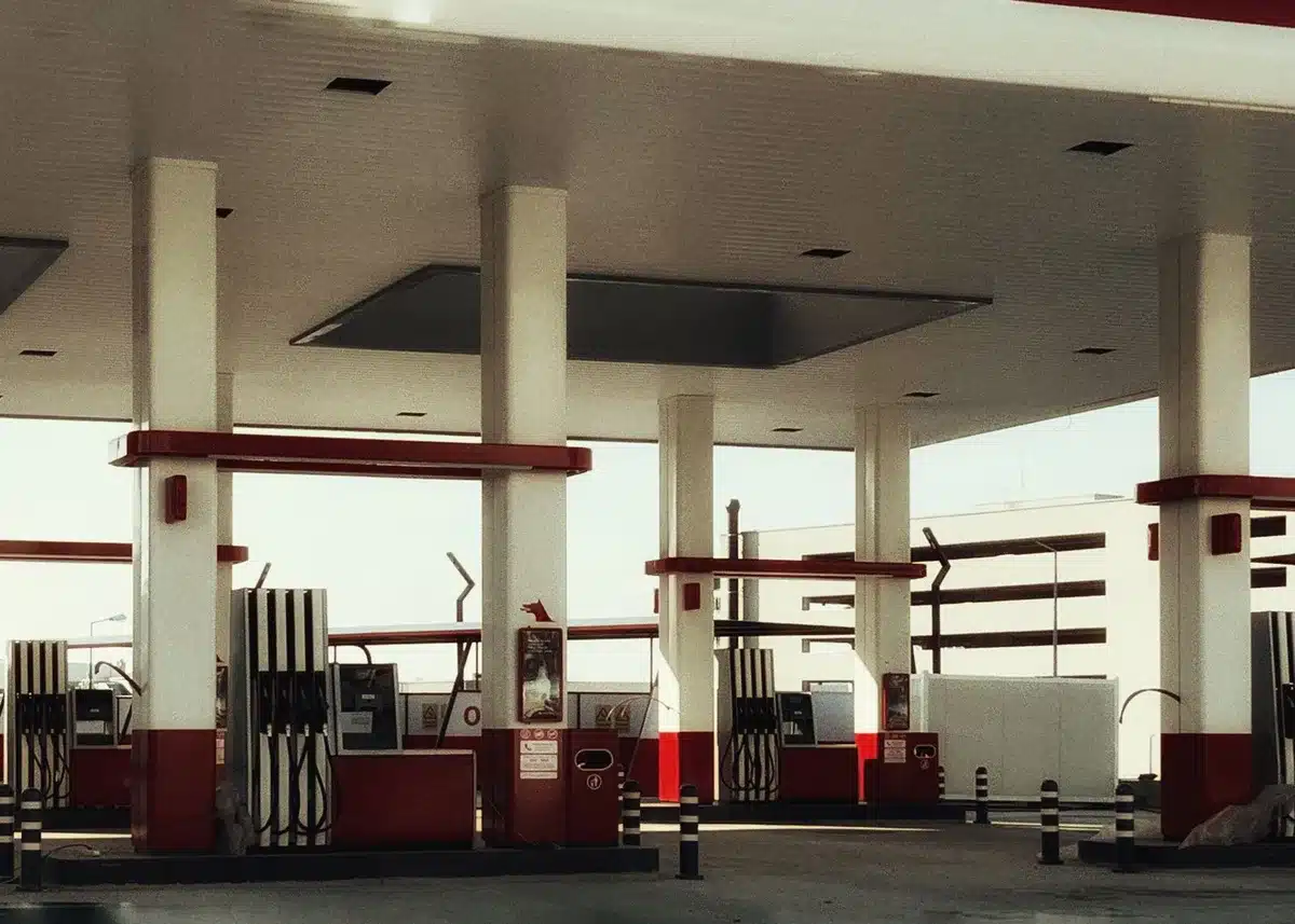A gas station pump display showing elevated prices, with a blurred figure in background looking at the numbers, conveying economic concern and frustration