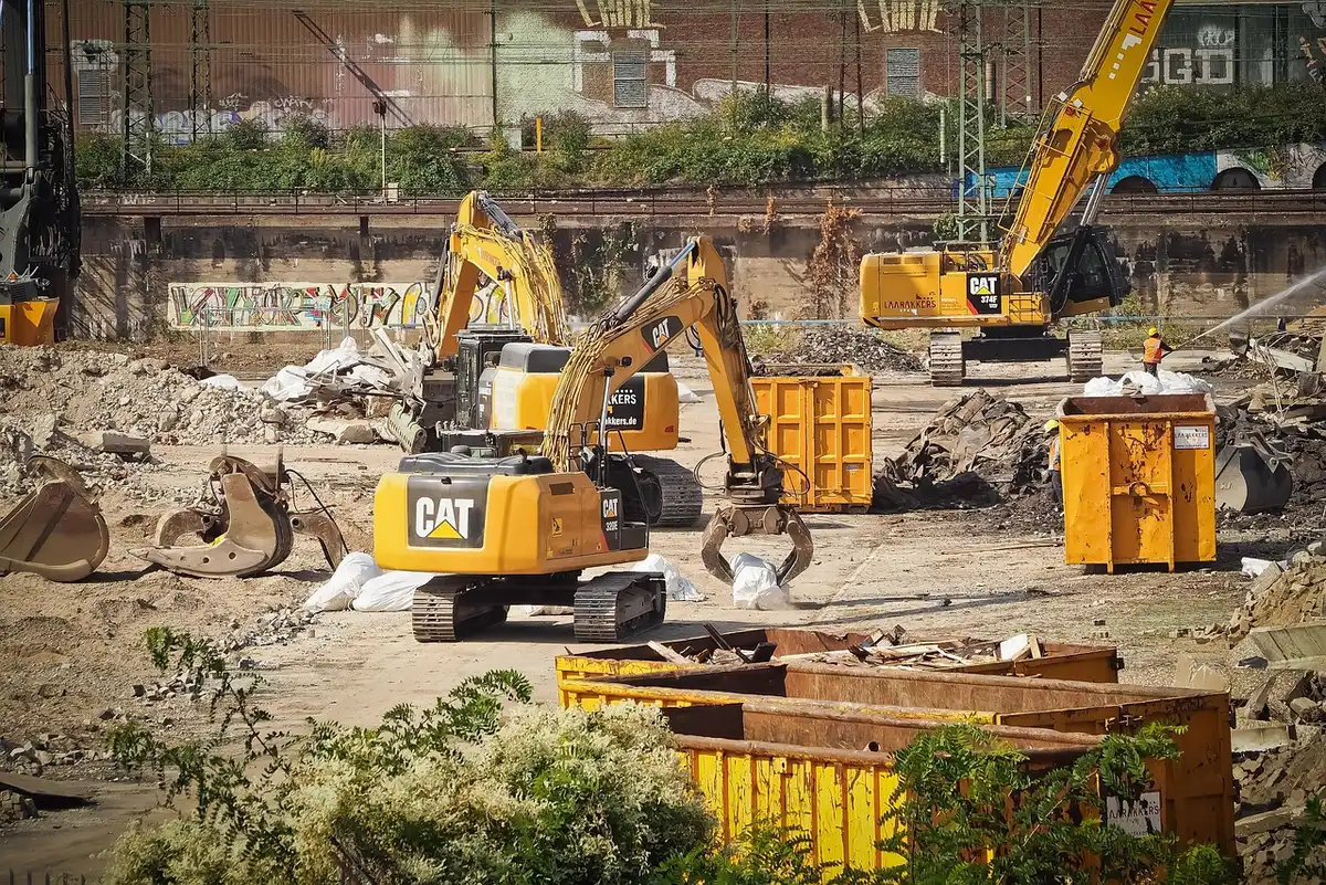 Construction cranes towering above white marble and limestone facades under clear sky, steel framework rising from excavation site, American flag visible on temporary structures