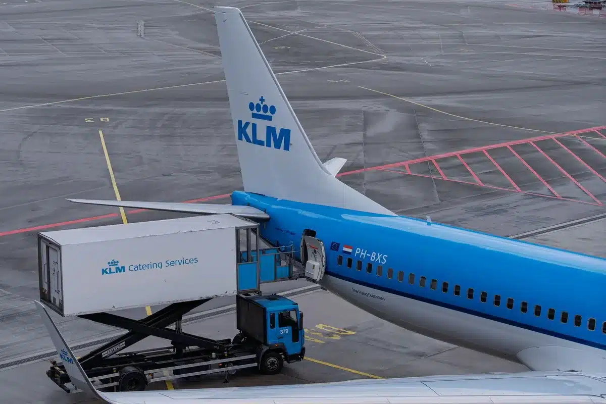 Tarmac at an international airport during daytime, an old Boeing 747 aircraft parked alongside a catering truck, security personnel visible in the distance, the scene capturing a moment of covert presidential movement