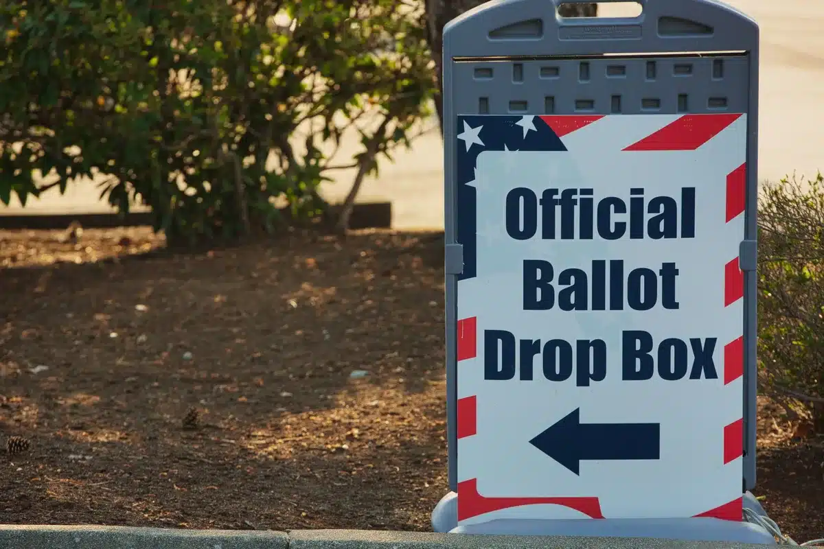 Ballot boxes in a voting precinct, election materials and voting booths visible, neutral civic setting