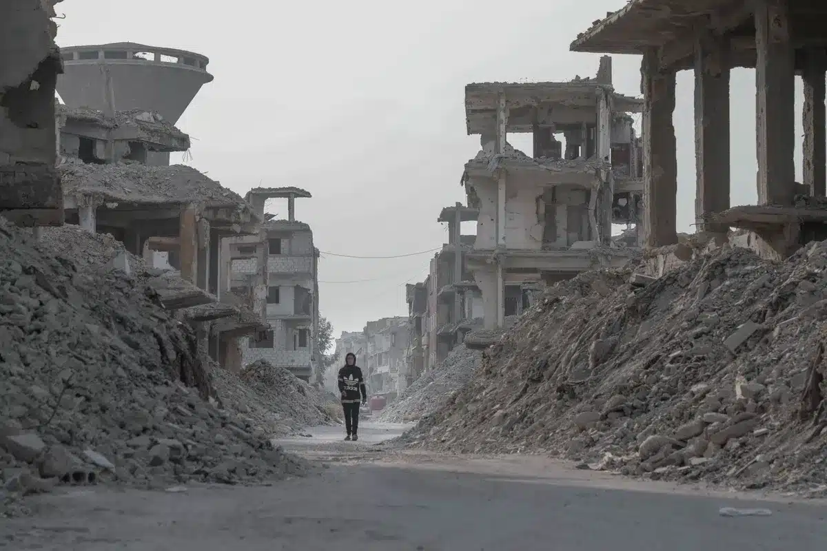 An empty Gaza street lined with damaged buildings, rubble scattered, an abandoned checkpoint or barrier visible, dust settling in afternoon light, no people visible, desolation and waiting evident.