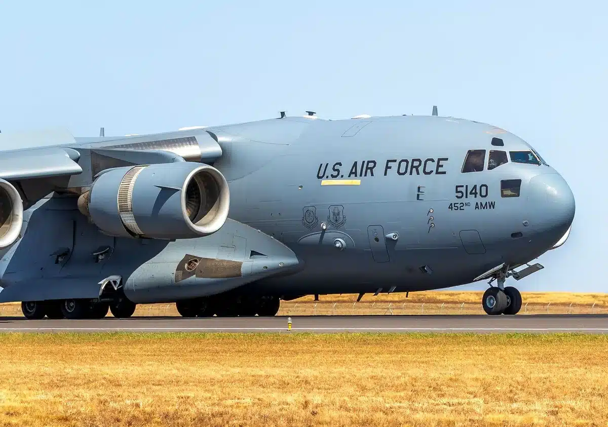 Military base perimeter at dusk, empty runway with warning lights, distant silhouettes of personnel in protective gear, sense of heightened alert and waiting