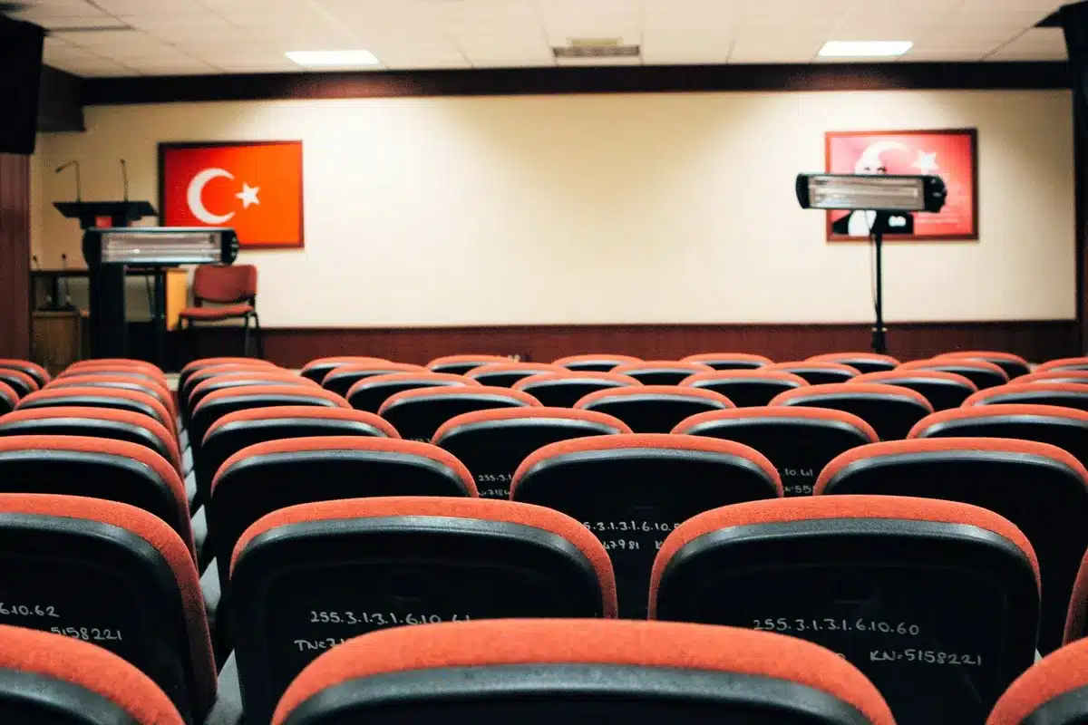 A formal government office setting with an empty conference table and chairs arranged for official meetings, sunlight streaming through tall windows, symbolizing institutional authority and organized decision-making.