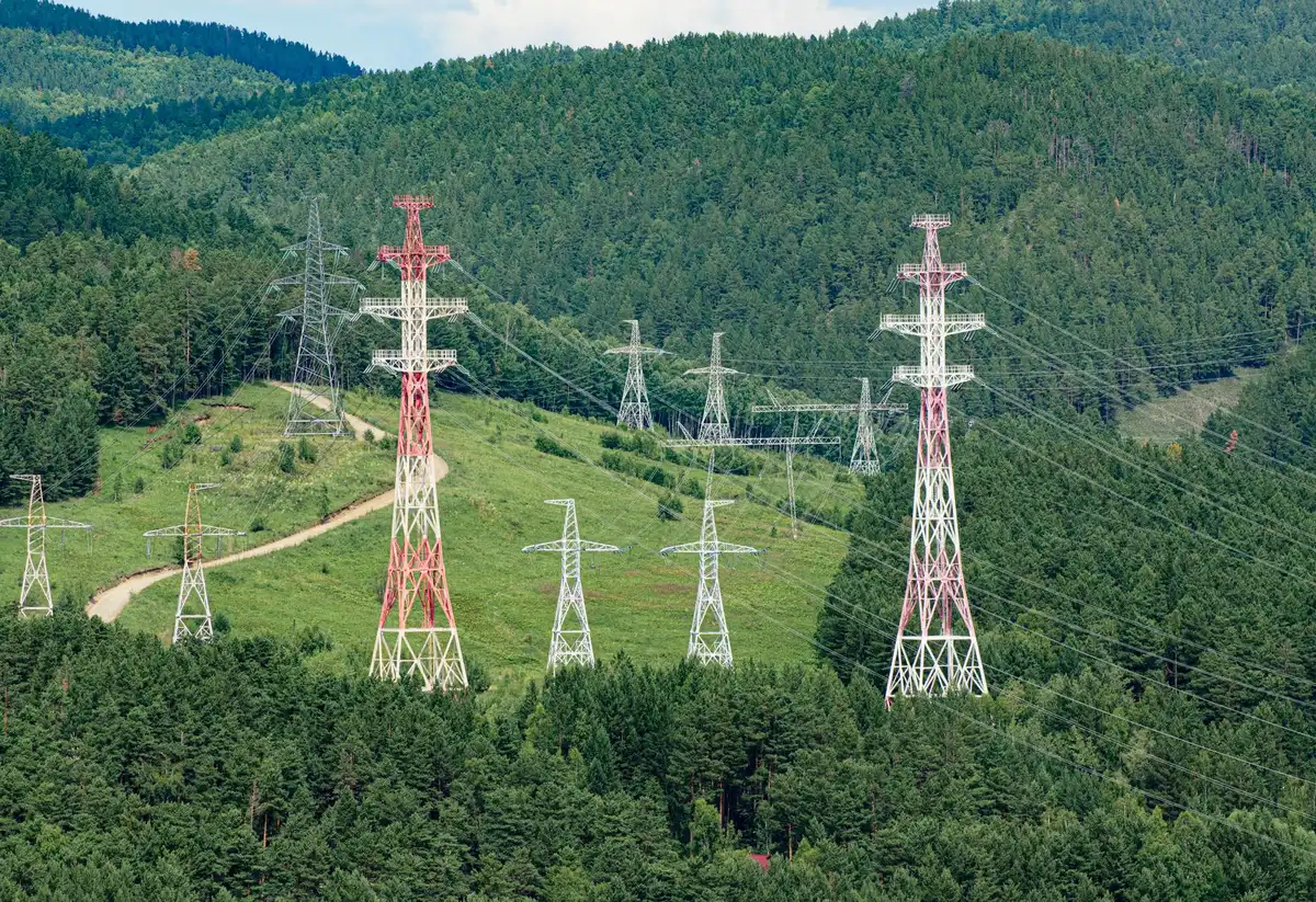 A power transmission switchyard and high-voltage infrastructure at a nuclear facility, with multiple transformers and transmission towers under bright sunlight, representing the grid infrastructure at risk.
