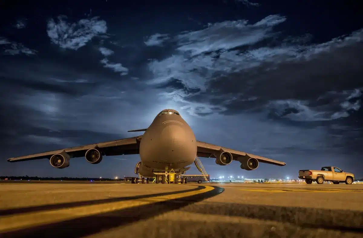 An airport terminal at night with runway lights glowing, silhouettes of security personnel in the foreground, suggesting heightened alert status