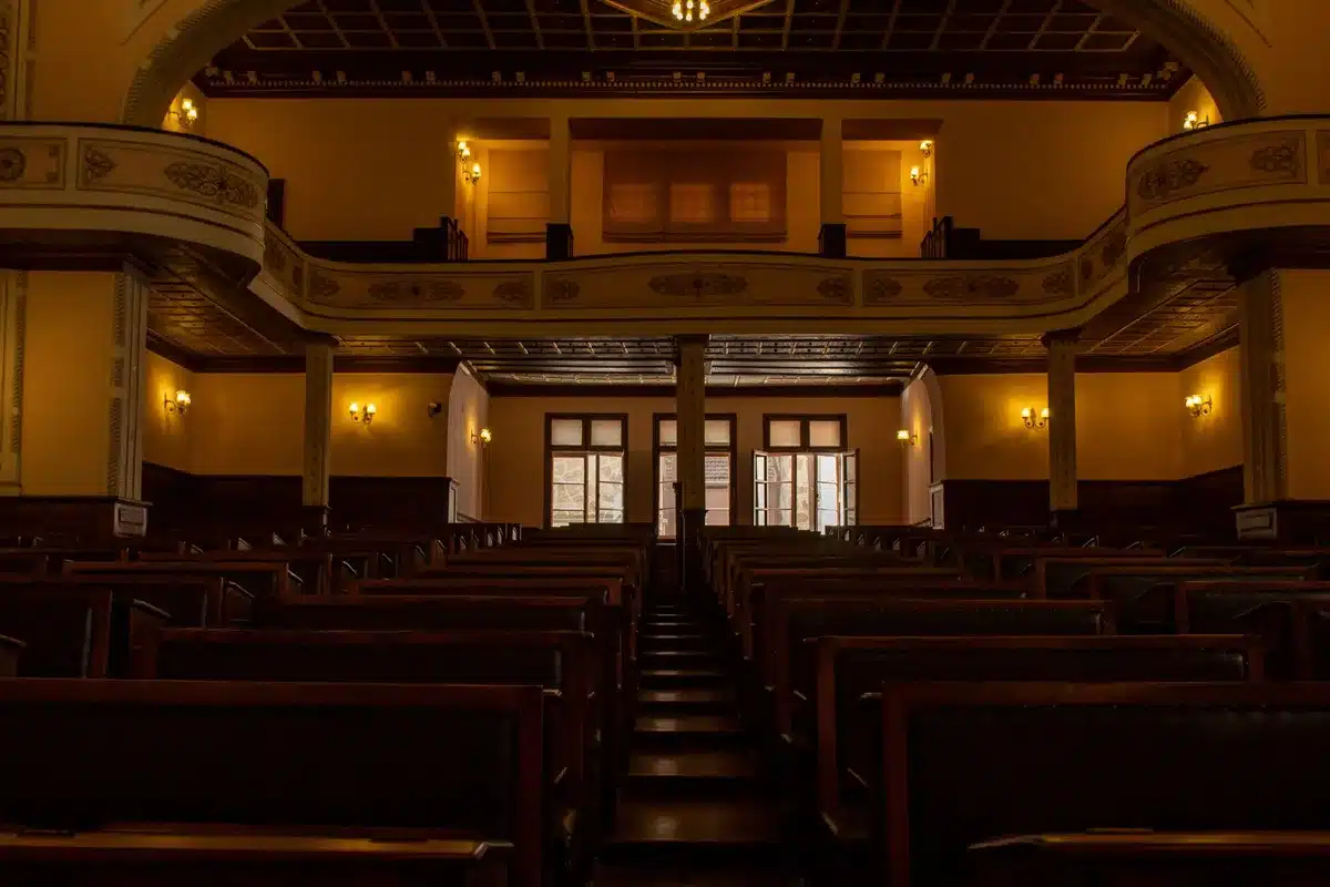 A formal courtroom interior with empty judge's bench and wooden desks, morning light filtering through tall windows, suggesting the weight of pending legal proceedings.
