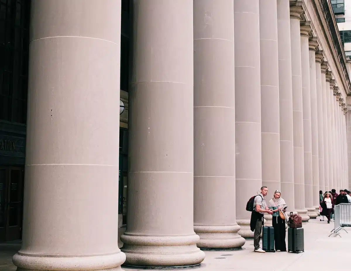 Federal courthouse entrance with classical columns and stone facade, a lone figure ascending the steps carrying a briefcase, gray morning light, serious architectural gravity